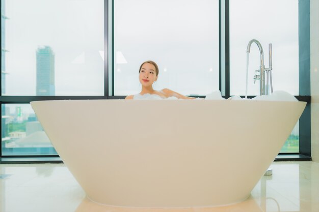 Retrato hermosa joven asiática relajarse sonrisa ocio en la bañera en el interior del baño