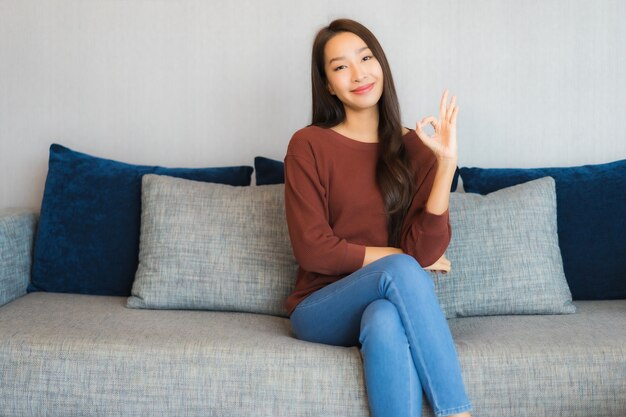 Retrato hermosa joven asiática relajarse sonrisa en el sofá en el interior de la sala de estar