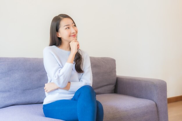 Retrato hermosa joven asiática relajarse sonrisa en el sofá en la sala de estar