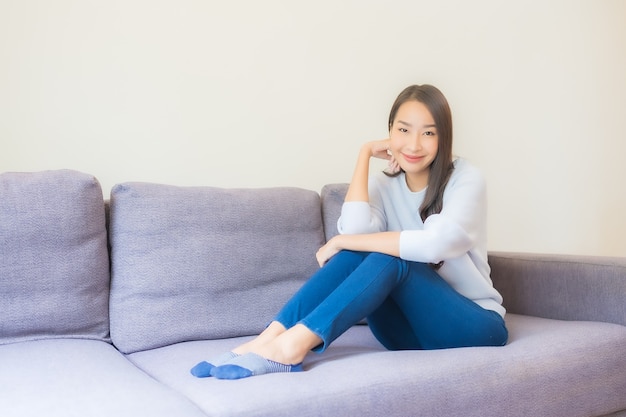Retrato hermosa joven asiática relajarse sonrisa en el sofá en la sala de estar