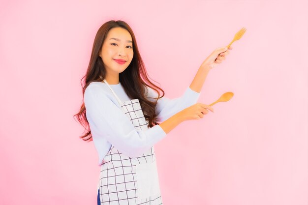 Retrato hermosa joven asiática en ropa de cocina con delantal en rosa pared aislada