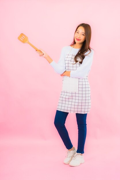 Retrato hermosa joven asiática en ropa de cocina con delantal en rosa pared aislada