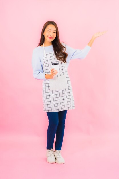 Retrato hermosa joven asiática en ropa de cocina con delantal en rosa pared aislada