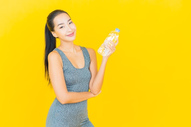 Retrato hermosa joven asiática con ropa deportiva y botella de agua en la pared amarilla