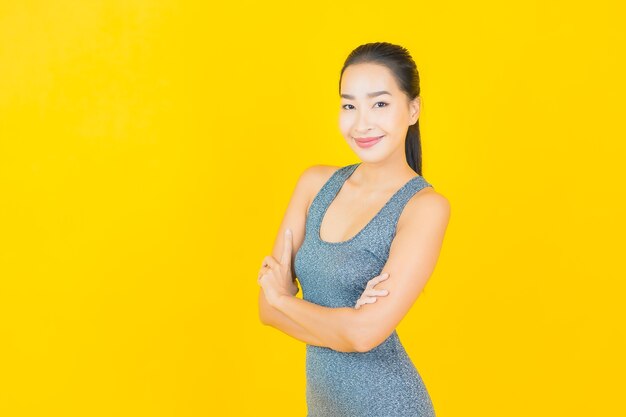 Retrato hermosa joven asiática con ropa deportiva lista para hacer ejercicio en la pared amarilla