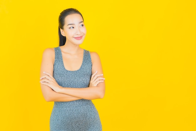 Retrato hermosa joven asiática con ropa deportiva lista para hacer ejercicio en la pared amarilla