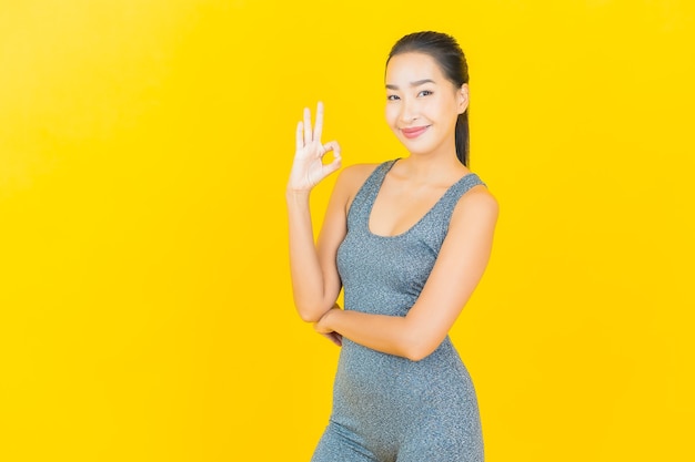 Retrato hermosa joven asiática con ropa deportiva lista para hacer ejercicio en la pared amarilla