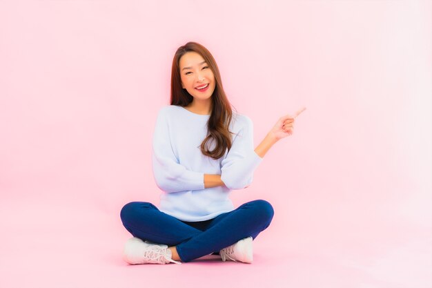 Retrato hermosa joven asiática sentada en el piso con pared aislada de color rosa