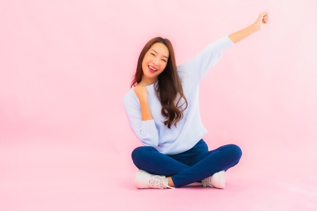 Retrato hermosa joven asiática sentada en el piso con pared aislada de color rosa