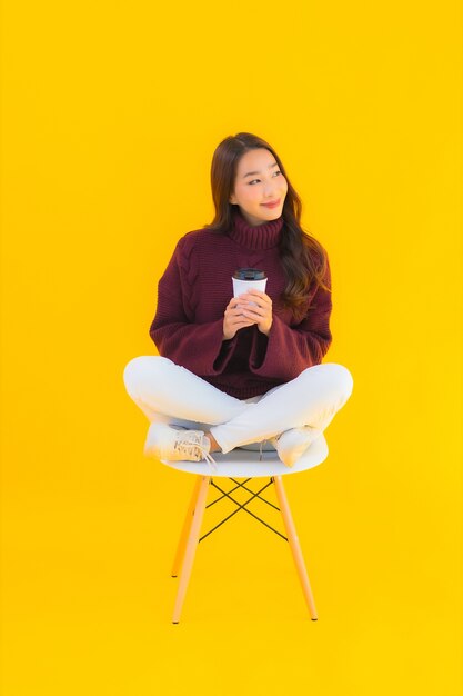 Retrato hermosa joven asiática sentarse en una silla con fondo amarillo aislado