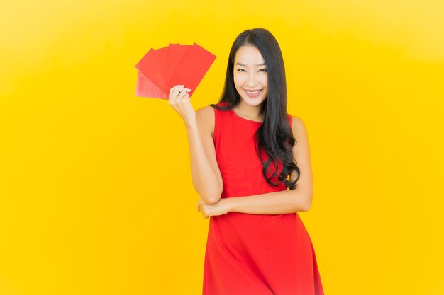 Retrato hermosa joven asiática con sobre rojo del año nuevo chino en la pared amarilla