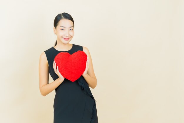 Retrato hermosa joven asiática sonríe con forma de almohada de corazón en la pared de color