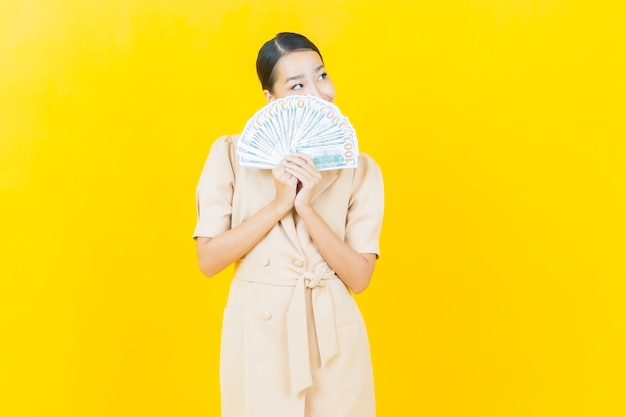 Retrato hermosa joven asiática sonríe con mucho dinero en efectivo y dinero en la pared de color