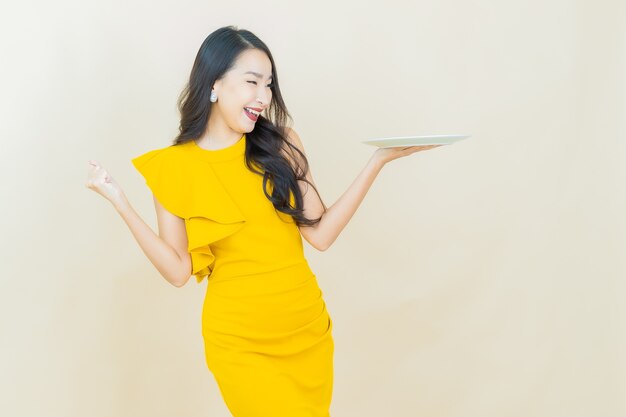 Retrato hermosa joven asiática sonríe con plato vacío en la pared beige