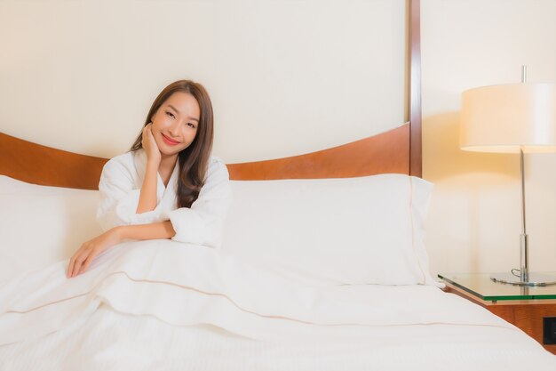 Retrato hermosa joven asiática sonríe relajante en la cama en el interior del dormitorio