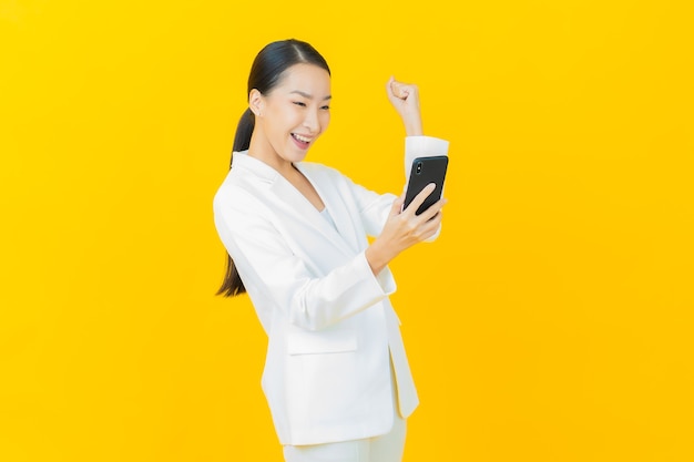 Retrato hermosa joven asiática sonríe con teléfono móvil inteligente en la pared de color