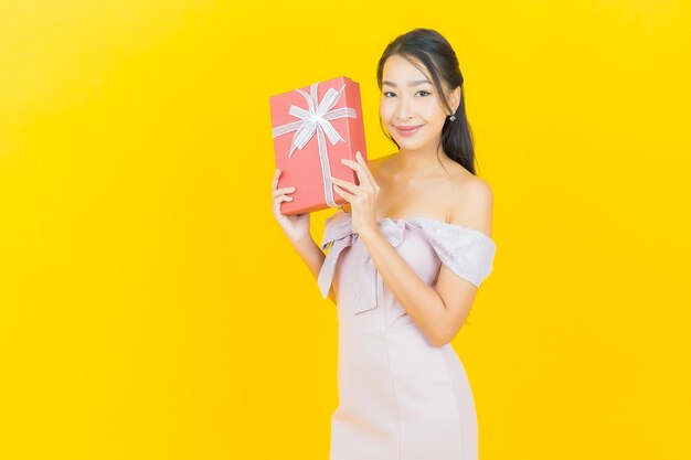 Retrato hermosa joven asiática sonriendo con caja de regalo roja en la pared de color
