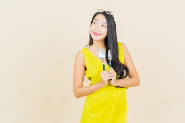 Retrato hermosa joven asiática sonrisa con cuchara y tenedor en la pared de color