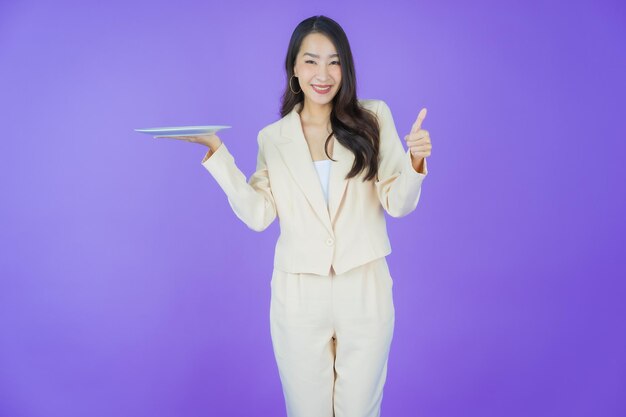 Retrato hermosa joven asiática sonrisa con plato vacío sobre fondo de color