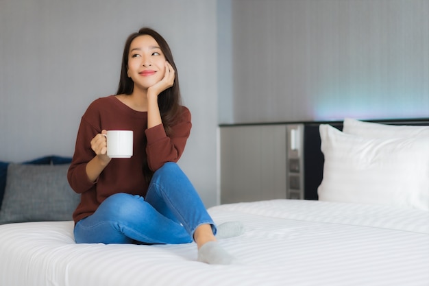 Retrato hermosa joven asiática con taza de café en la cama en el interior del dormitorio
