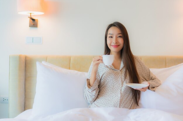 Retrato hermosa joven asiática con taza de café en la cama