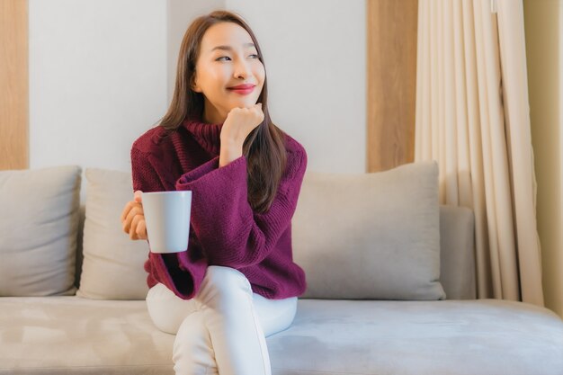 Retrato hermosa joven asiática con taza de café en el interior de la decoración del sofá de la sala de estar