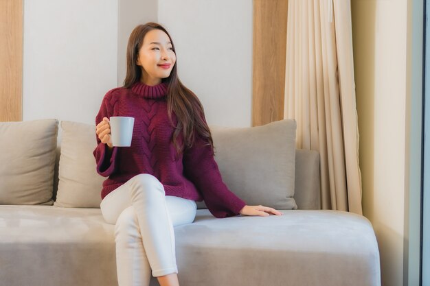 Retrato hermosa joven asiática con taza de café en el interior de la decoración del sofá de la sala de estar