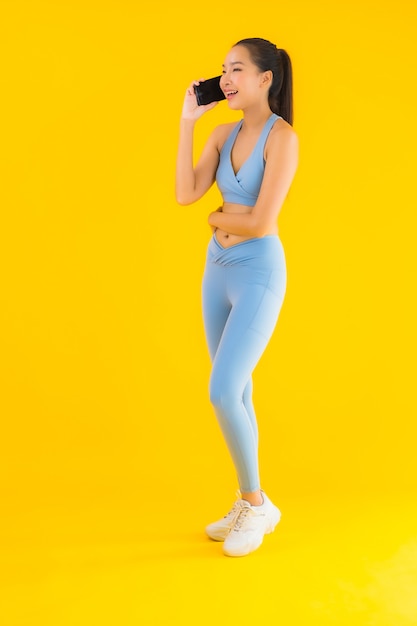 Retrato hermosa joven asiática con teléfono móvil inteligente en amarillo aislado