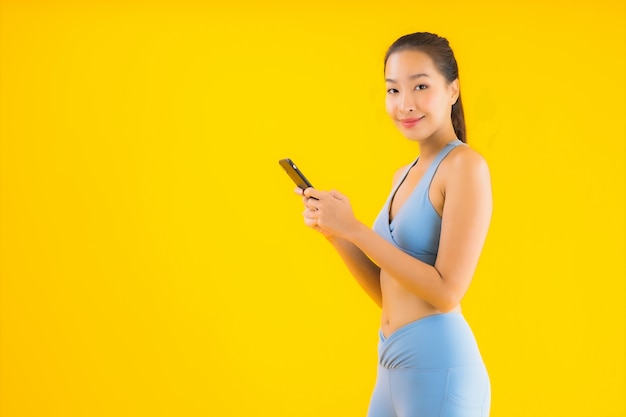 Retrato hermosa joven asiática con teléfono móvil inteligente en amarillo aislado