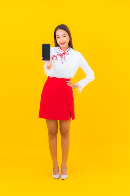 Retrato hermosa joven asiática con teléfono móvil inteligente en amarillo