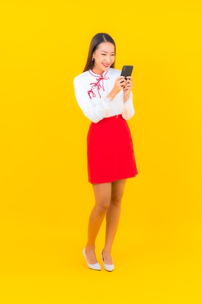 Retrato hermosa joven asiática con teléfono móvil inteligente en amarillo