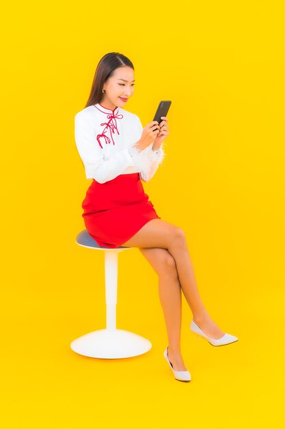 Retrato hermosa joven asiática con teléfono móvil inteligente en amarillo