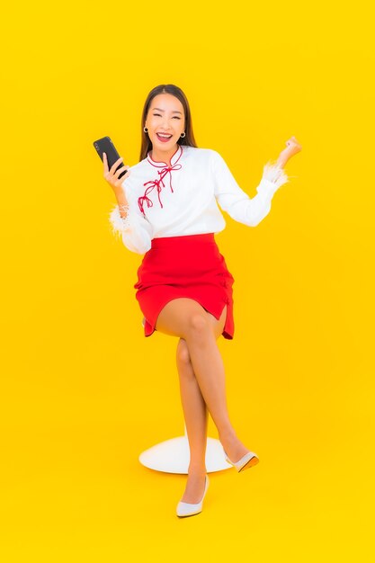 Retrato hermosa joven asiática con teléfono móvil inteligente en amarillo