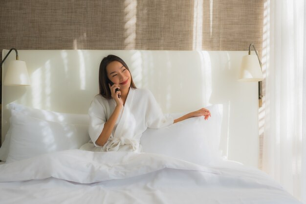 Retrato hermosa joven asiática con teléfono móvil inteligente en la cama en el dormitorio