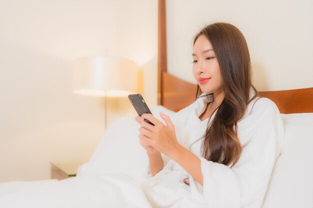 Retrato hermosa joven asiática con teléfono móvil inteligente en la cama en el interior del dormitorio