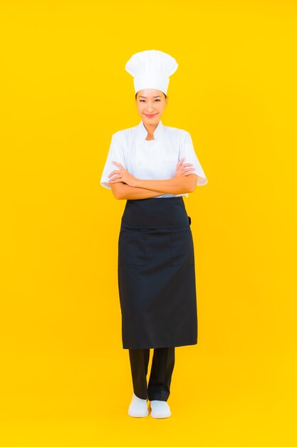 Retrato de una hermosa joven asiática en uniforme de chef o cocinero con sombrero en un fondo aislado amarillo