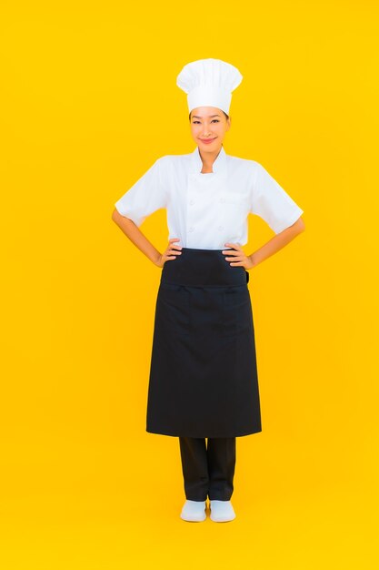 Retrato hermosa joven asiática en uniforme de cocinero o cocinero con sombrero sobre fondo amarillo aislado