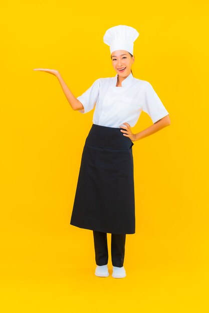 Retrato hermosa joven asiática en uniforme de cocinero o cocinero con sombrero sobre fondo amarillo aislado