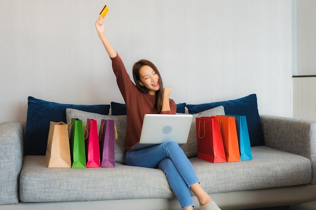 Retrato hermosa joven asiática usa computadora portátil y tarjeta de crédito para compras en línea en el sofá en el interior de la sala de estar