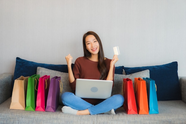 Retrato hermosa joven asiática usa computadora portátil y tarjeta de crédito para compras en línea en el sofá en el interior de la sala de estar