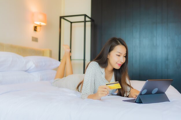 Retrato hermosa joven asiática usa tableta con tarjeta de crédito en la cama