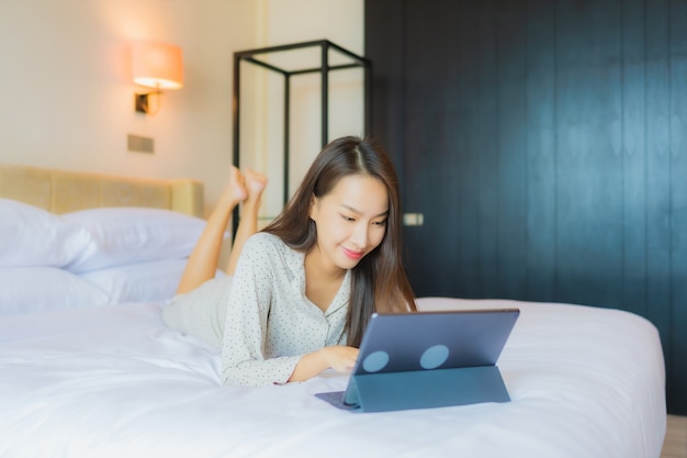 Retrato hermosa joven asiática usa tableta con tarjeta de crédito en la cama