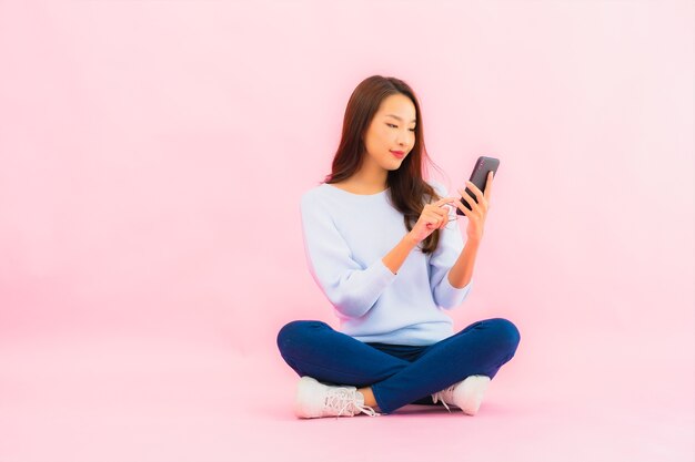 Retrato hermosa joven asiática usa teléfono móvil inteligente en pared aislada de color rosa