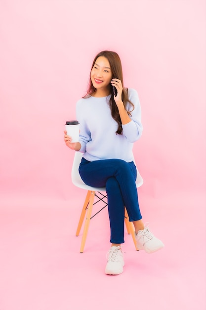 Retrato hermosa joven asiática usa teléfono móvil inteligente en pared aislada de color rosa
