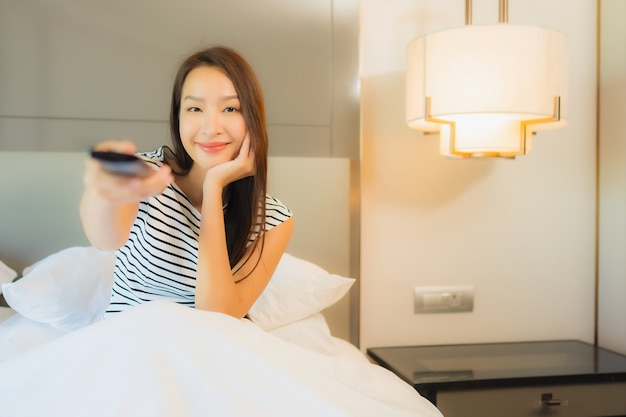 Retrato hermosa joven asiática usa tv remota en la cama en el interior del dormitorio