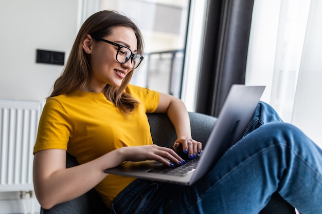 Retrato hermosa joven asiática usando laptop para trabajar y sentarse en un sillón en el área de la sala de estar