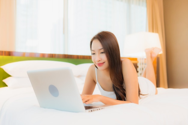 Retrato hermosa joven asiática usar computadora portátil en la cama en el interior del dormitorio