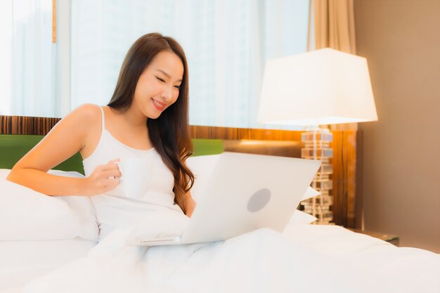 Retrato hermosa joven asiática usar computadora portátil en la cama en el interior del dormitorio