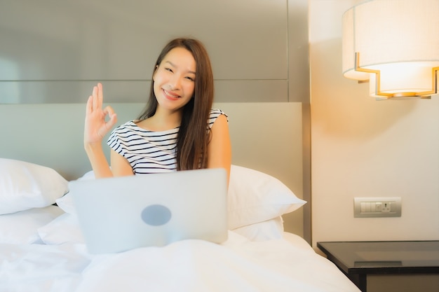 Retrato hermosa joven asiática usar computadora portátil en la cama en el interior del dormitorio