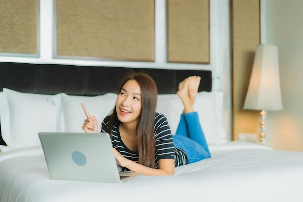 Retrato hermosa joven asiática usar computadora portátil en la cama en el interior del dormitorio